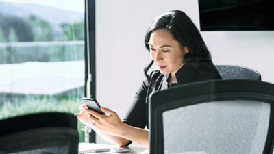 Pessoa sentada em uma mesa de confer&ecirc;ncia olhando para um celular